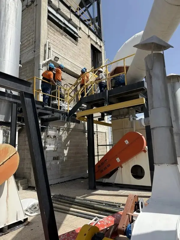 Cuadrilla con casco trabajando en plataformas de planta industrial